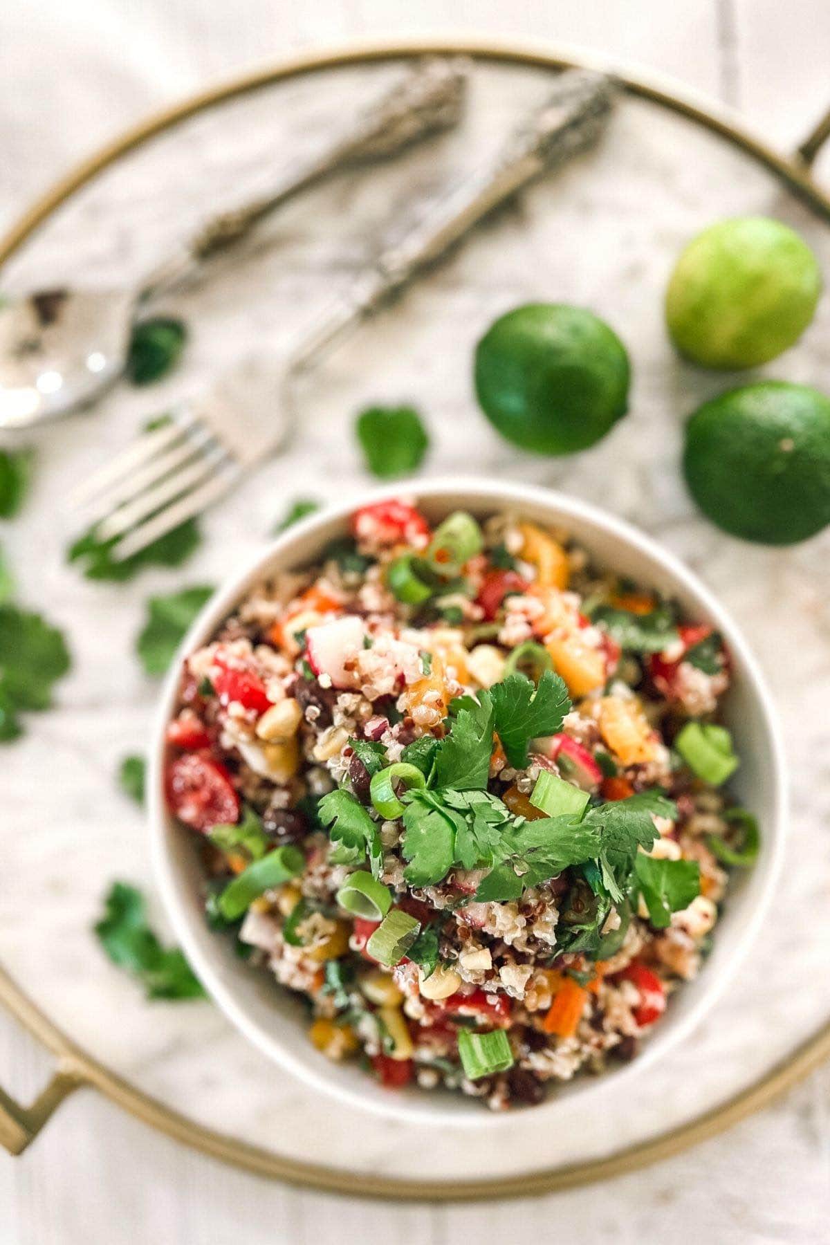Overhead shot of a white bowl with black bean and quinoa salad. Forks and limes in the background.