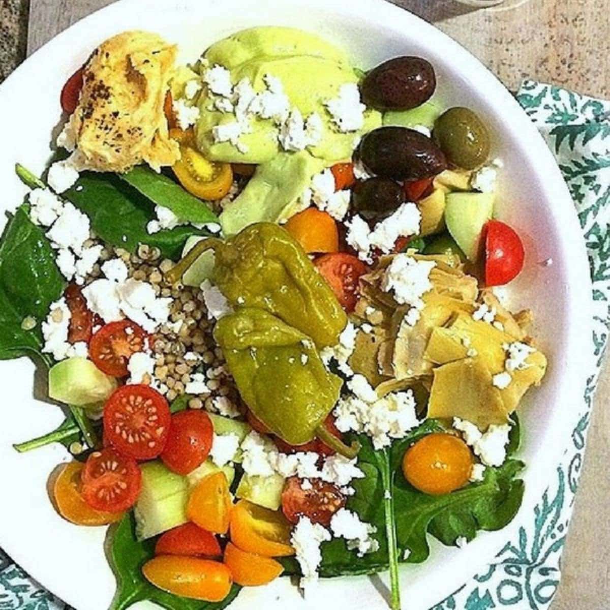 Mediterranean grain bowl in a white bowl with colorful vegetables and feta cheese on top.