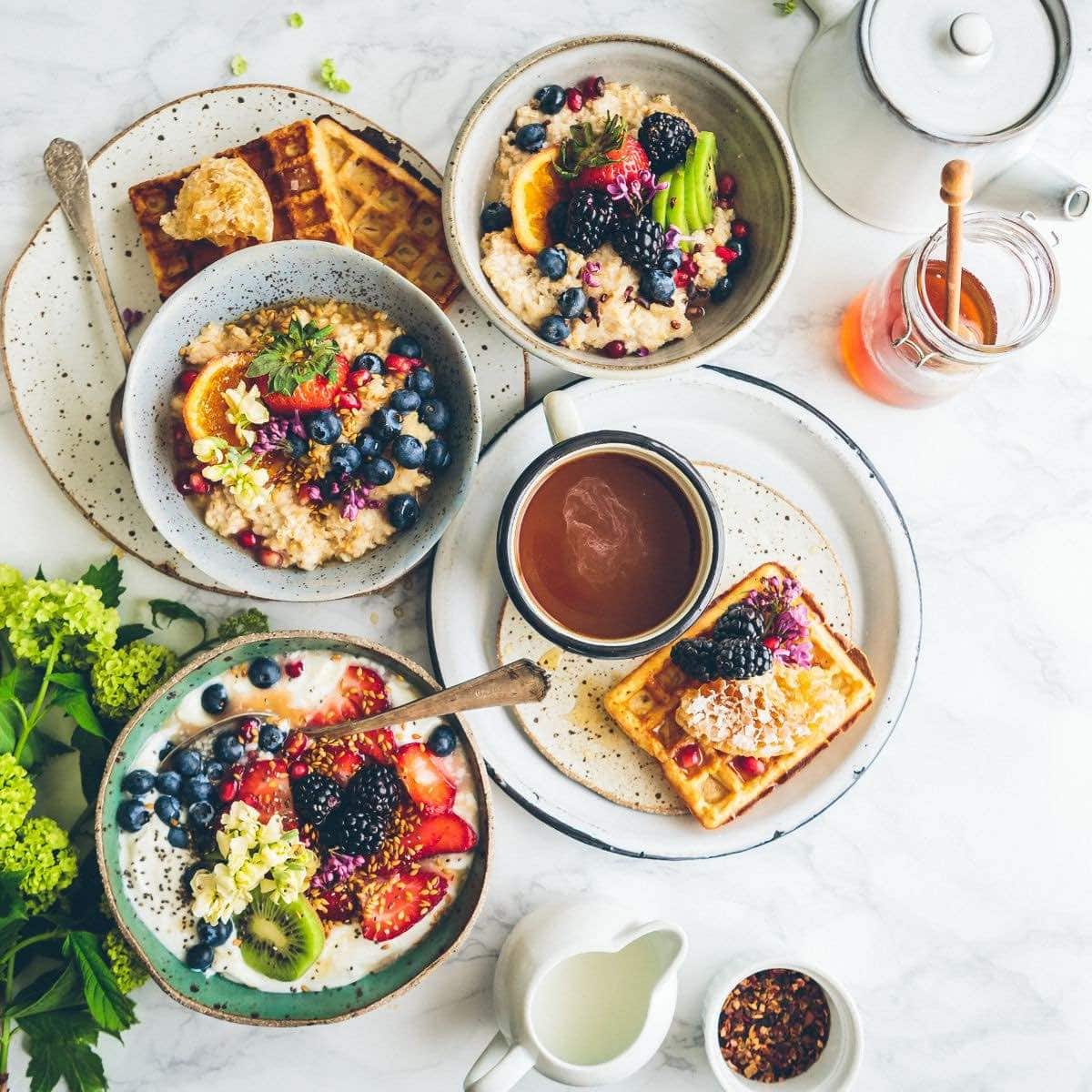 Overhead photo of oatmeal bowls and waffles topped with fruit and flowers.