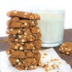 Stack of sweet potato cookies with white chocolate chips on a white napkin and a glass of milk in the background.
