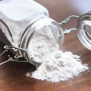 Square up close photo of gluten-free flour spilling out of a glass jar.