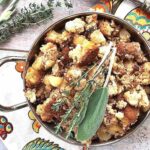 Overhead photo of gluten free stuffing recipe in a stainless steel bowl with rosemary and sage on top.