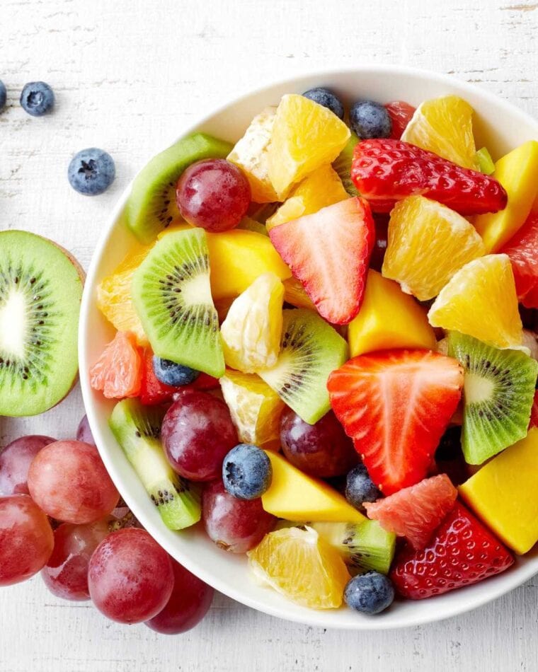 White bowl filled with kiwi fruit, strawberries, blueberries, oranges, and grapes.