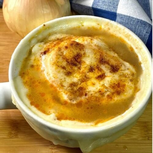 White bowl with gluten-free French onion soup on a wooden board.