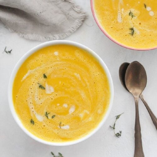 Two bowls of ginger carrot soup with fresh herbs on top.