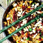 Bowl of fried rice with pine nuts and sriracha on top. Green jade chopsticks on top of the bowl.