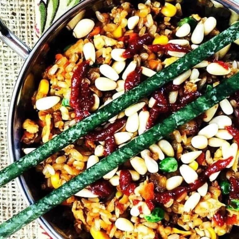 Bowl of fried rice with pine nuts and sriracha on top. Green jade chopsticks on top of the bowl.