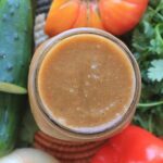 Overhead photo of a glass of homemade vegetable juice in a mason jat surrounded by cucumber, tomato, onion, and cilantro.