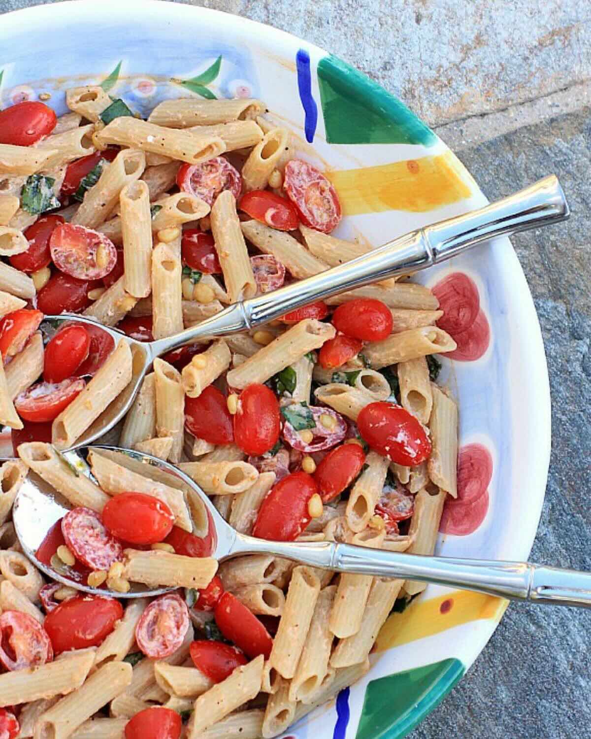 Pasta with tomatoes, basil, and pine nuts in a colorful serving bowl.