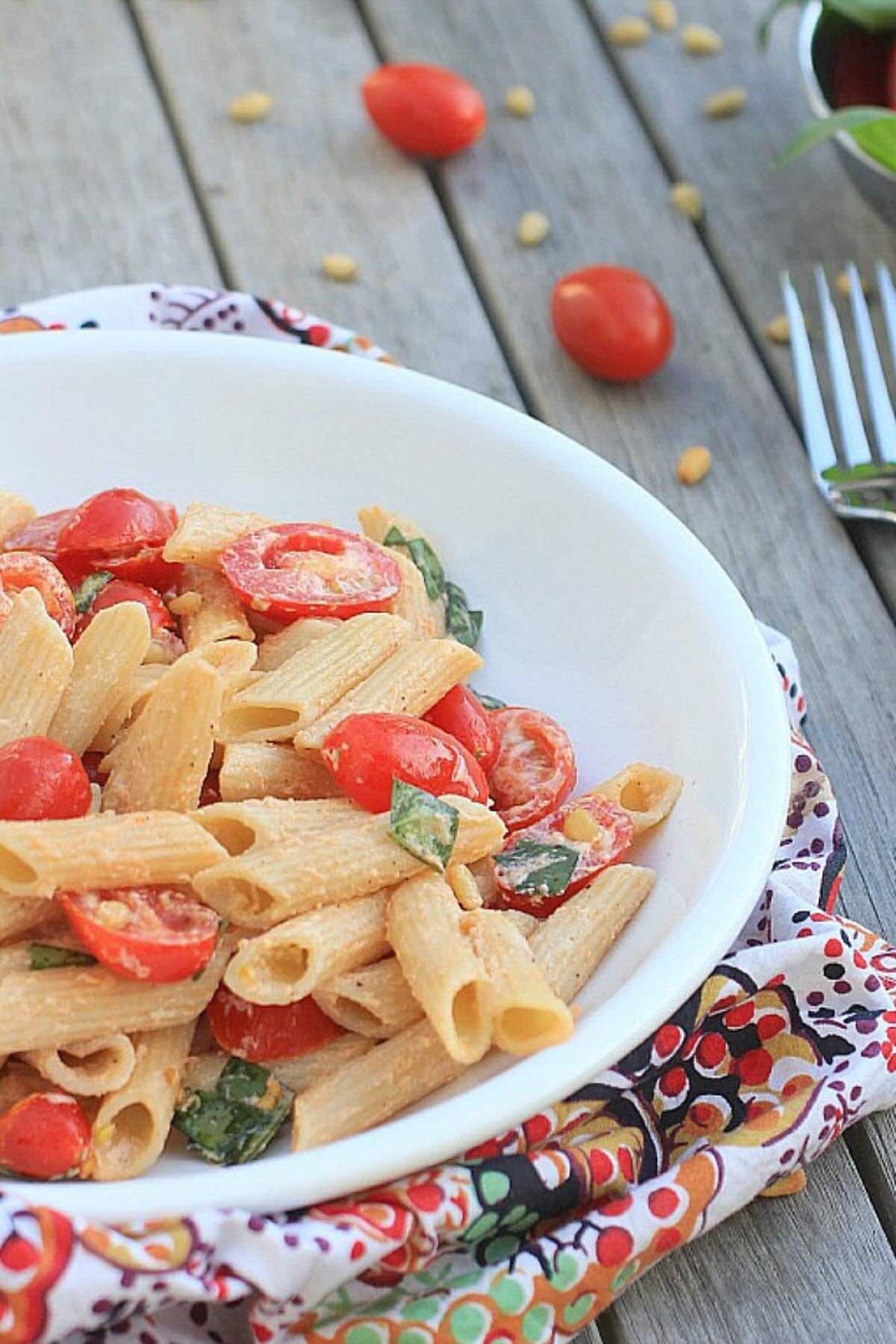 White bowl with gluten free pasta salad with tomatoes, basil, ricotta cheese, and pine nuts.