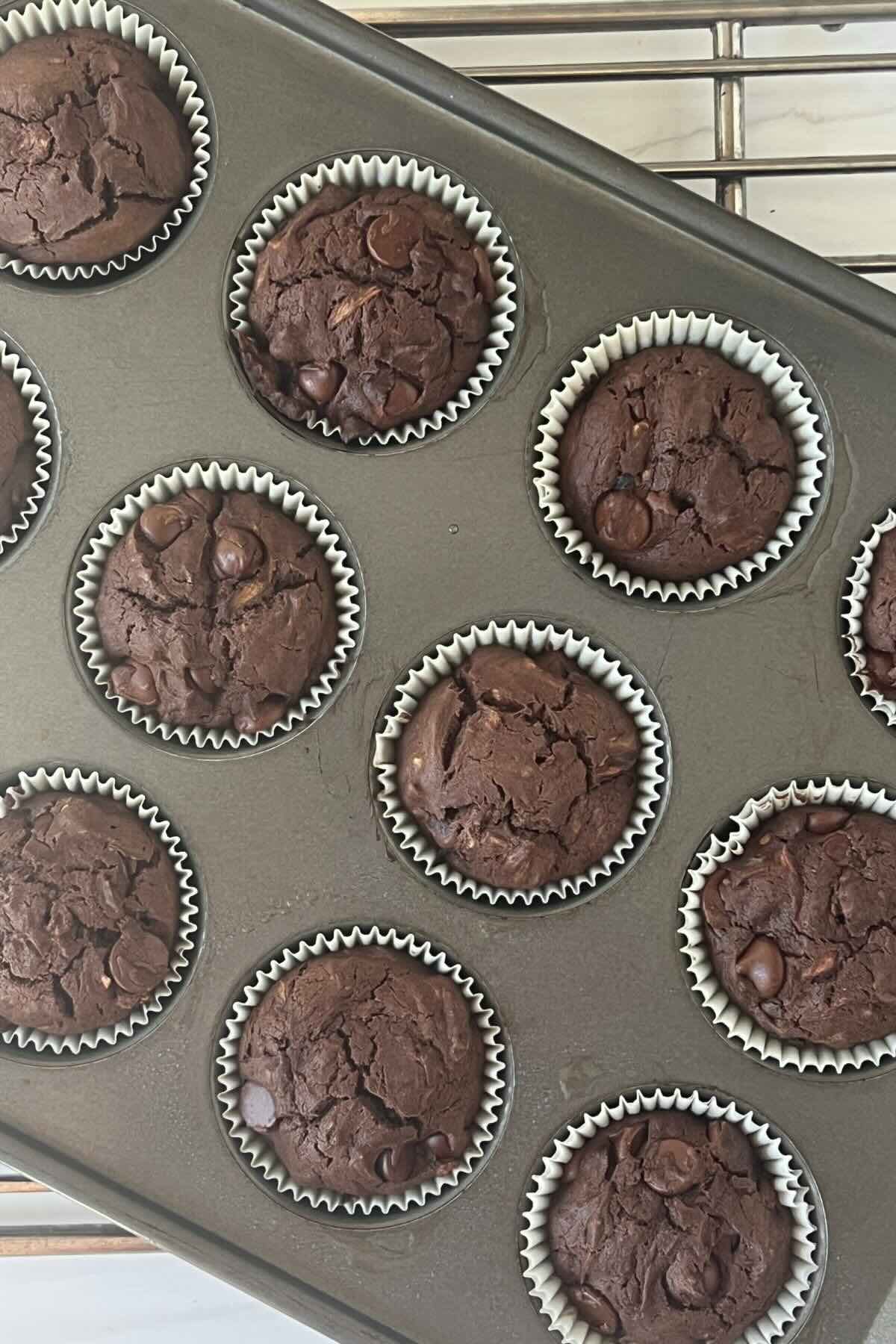 Gluten free chocolate zucchini muffins in white liners in a cupcake baking sheet.