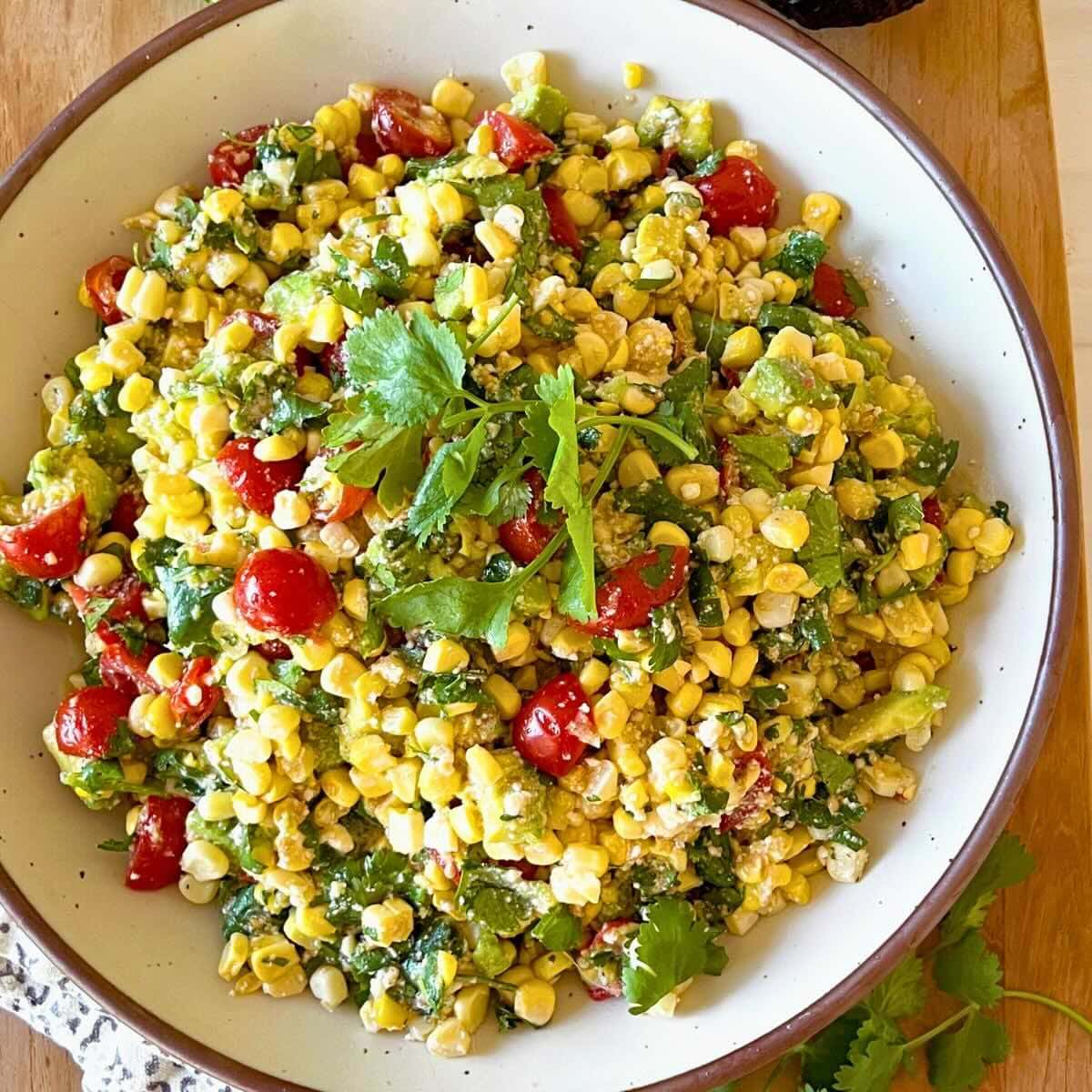 Avocado corn salad with tomato topped with cilantro in a rustic white East Fork pottery bowl.