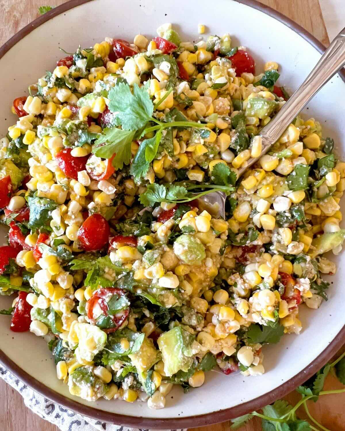 Close up photo of corn avocado salad in a white bowl with a serving spoon.