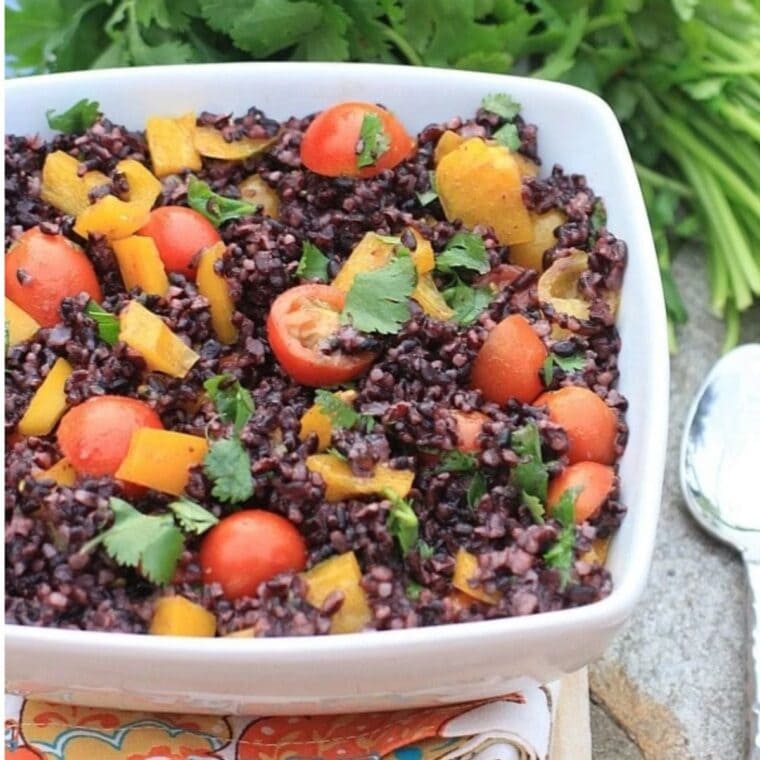 Black rice salad with cherry tomatoes, yellow bell peppers, and cilantro in a white serving bowl.