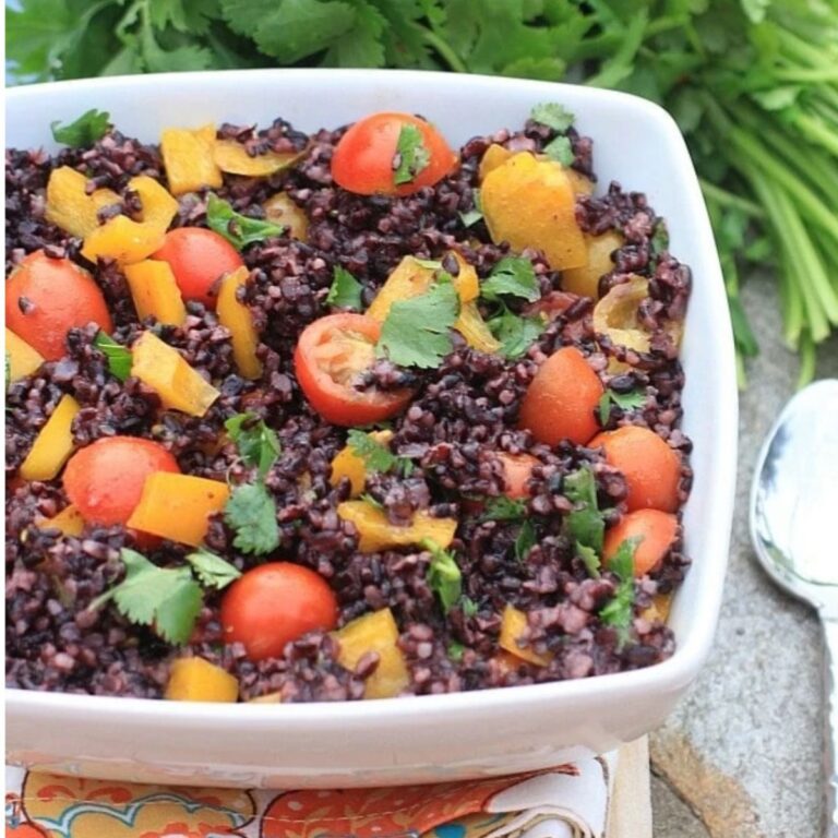 Black rice salad with cherry tomatoes, yellow bell peppers, and cilantro in a white serving bowl.