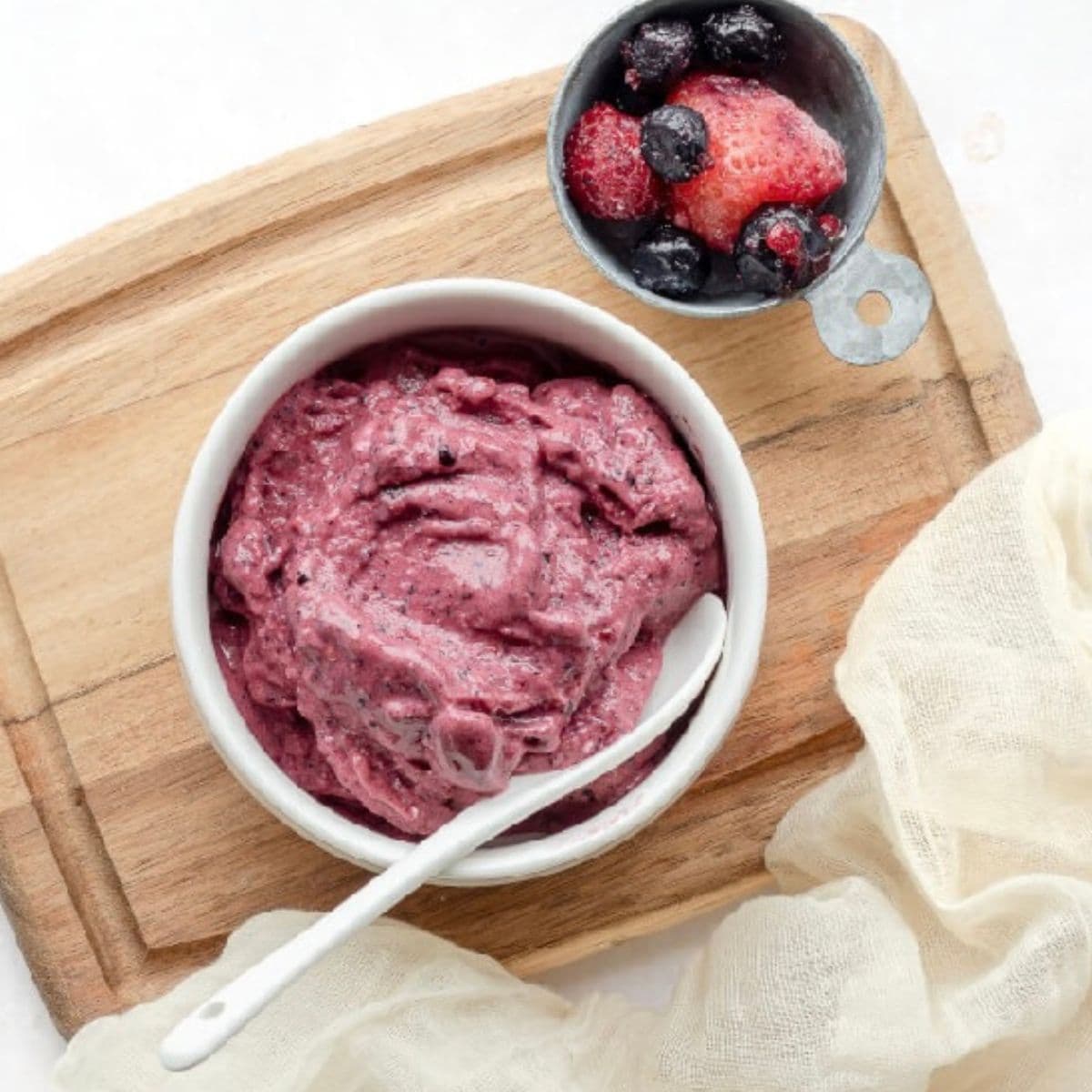 Bowl of berry frozen yogurt on a cutting board. Bowl of strawberries in the background.