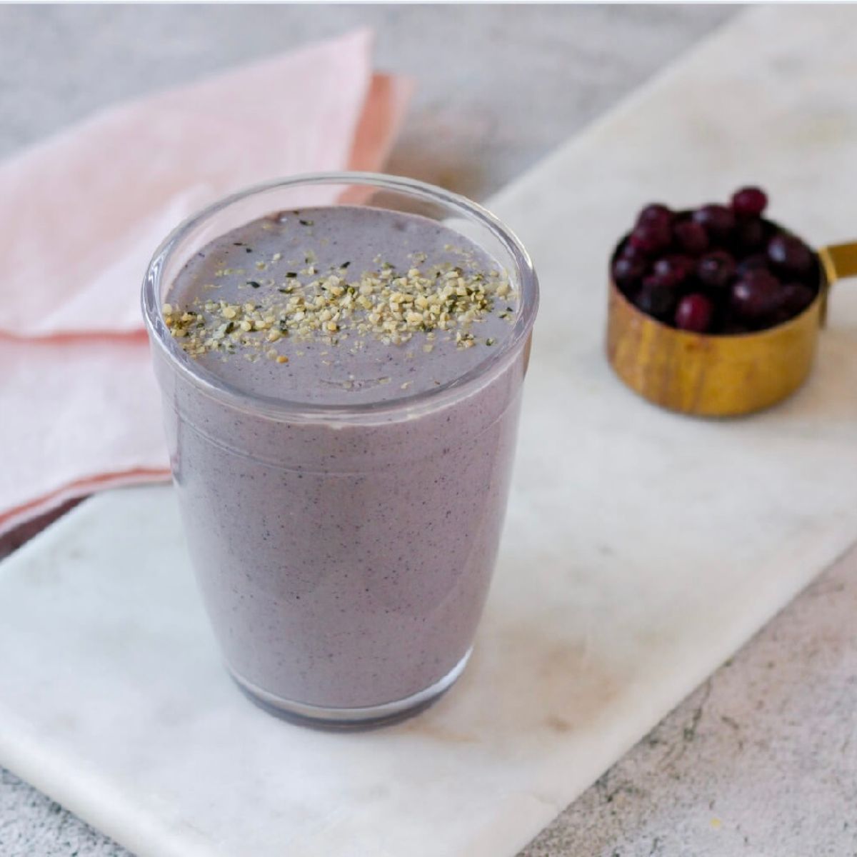 Blueberry smoothie on a white marble tray. Blueberries and a pink napkin in the background.