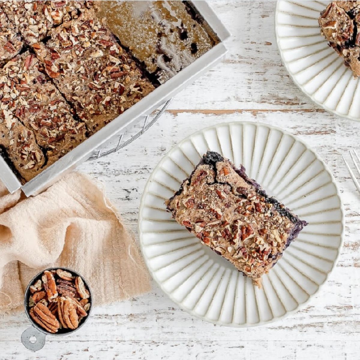 Overhead photo of baked blueberry oatmeal on a white plate with a tray of baked oatmeal in the background.