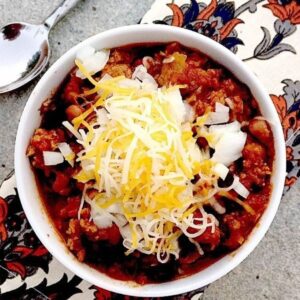 Gluten Free Chili in a white bowl topped with onions and cheese.