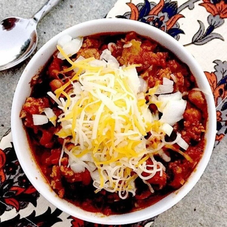 Gluten Free Chili in a white bowl topped with onions and cheese.