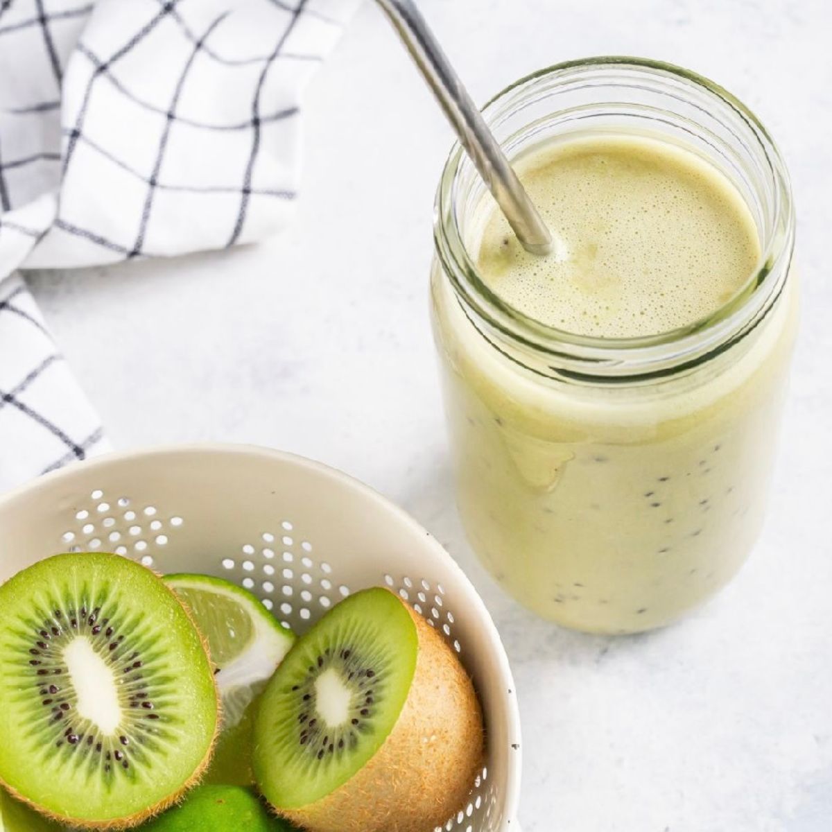 Green smoothie in a mason jar. Bowl of kiwi fruit on the side.