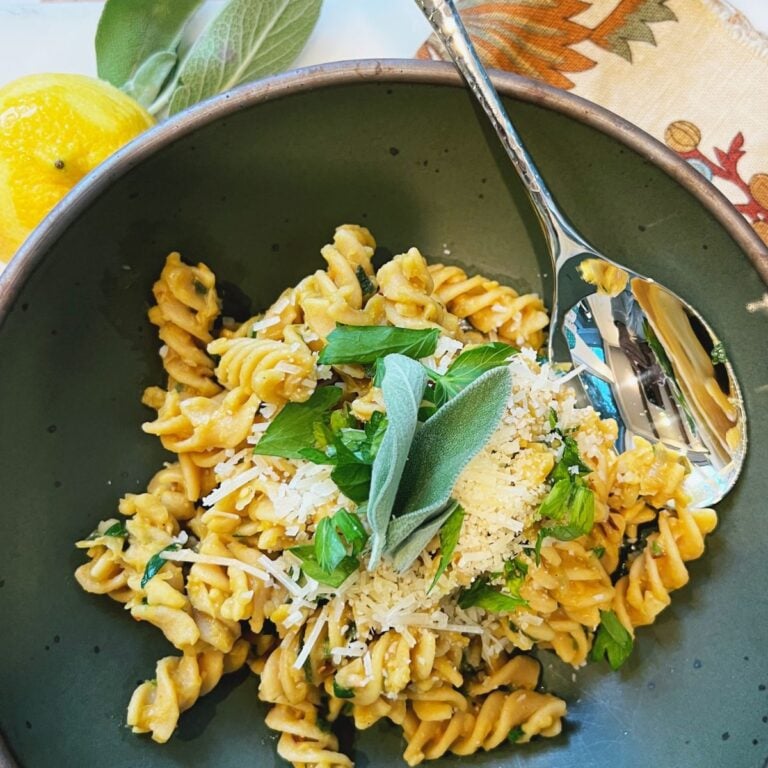 Green bowl filled with rotini pasta topped with parsley, sage, and Parmesan cheese.