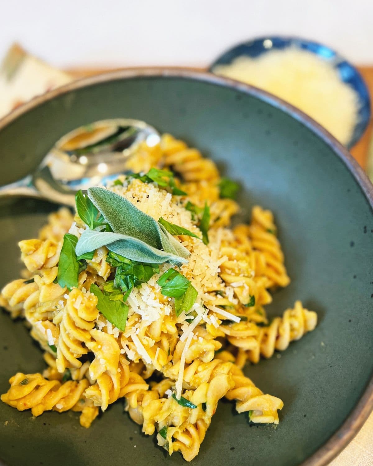 Close up photo of a green bowl filled with rotini pasta topped with parsley, sage, and Parmesan cheese.
