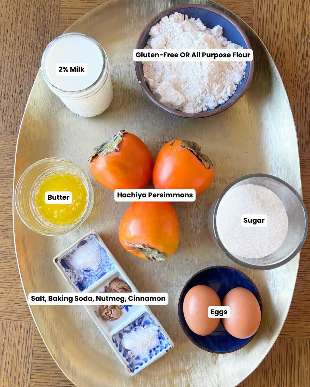 Gold platter with ingredients including: persimmons, milk, gluten free flour, sugar, eggs, butter, salt, baking soda, nutmeg, and cinnamon.