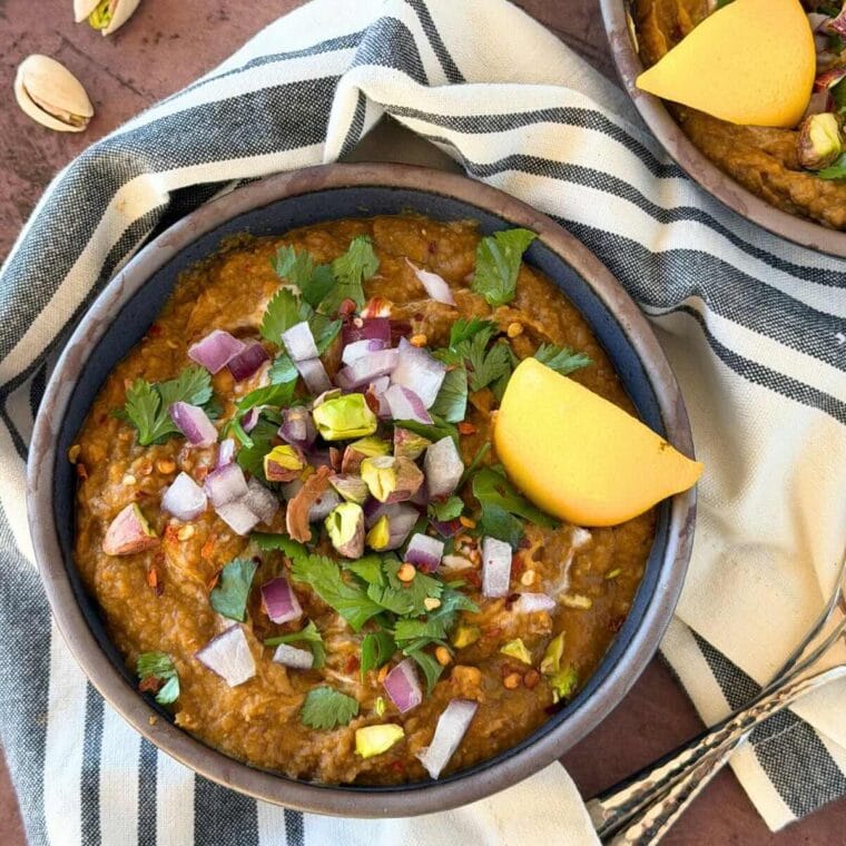 Carrot and lentil soup, topped with pistachios, red onion, cilantro, and red pepper flakes, in a dark blue bowl.