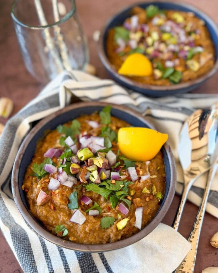 Carrot and lentil soup, topped with pistachios, red onion, cilantro, and red pepper flakes, in a dark blue bowl.