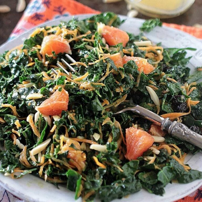 Kale salad topped with shredded carrots and orange sections on a white plate.