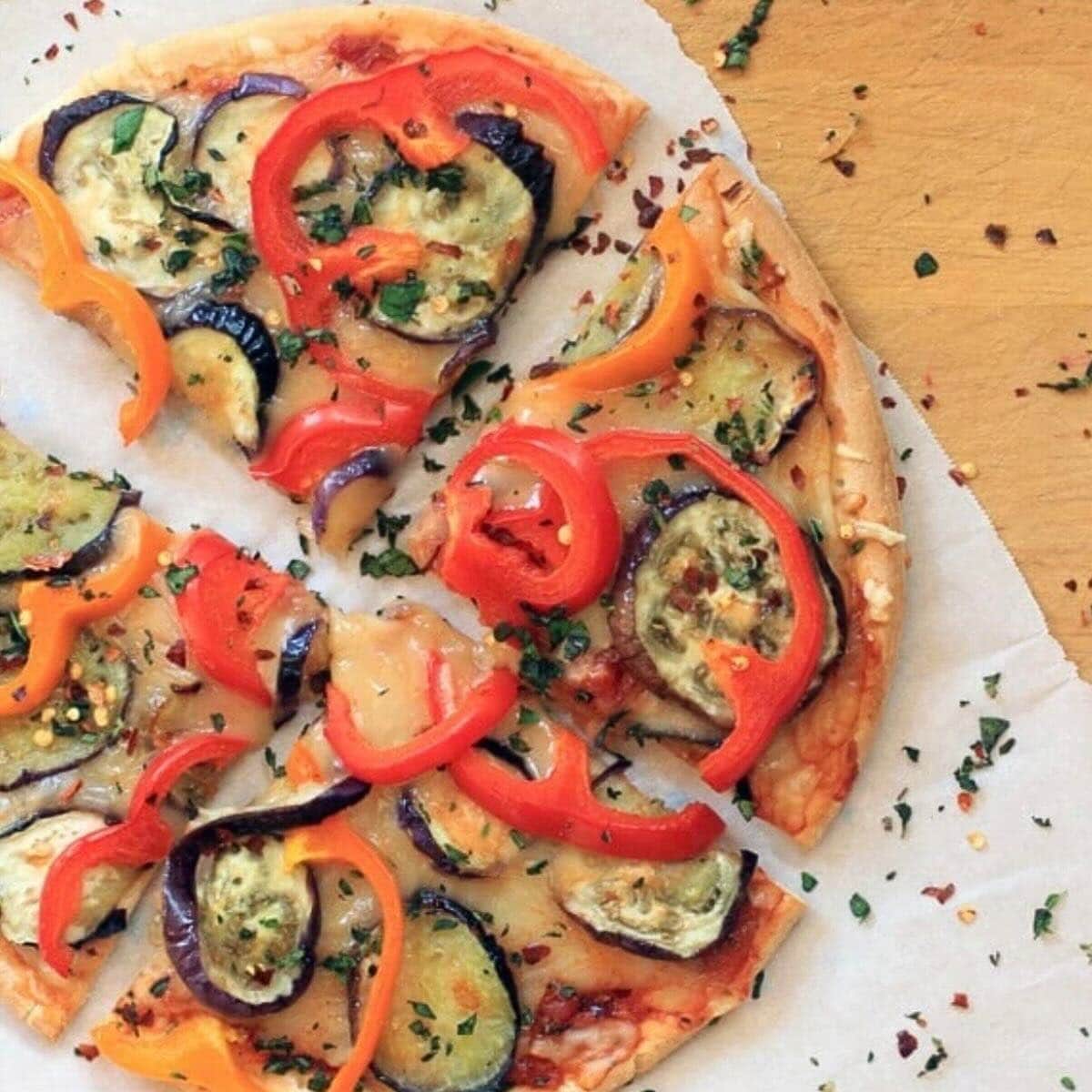 Overhead shot of a gluten free pizza crust topped with eggplant, bell peppers, fresh herbs, and cheddar cheese.